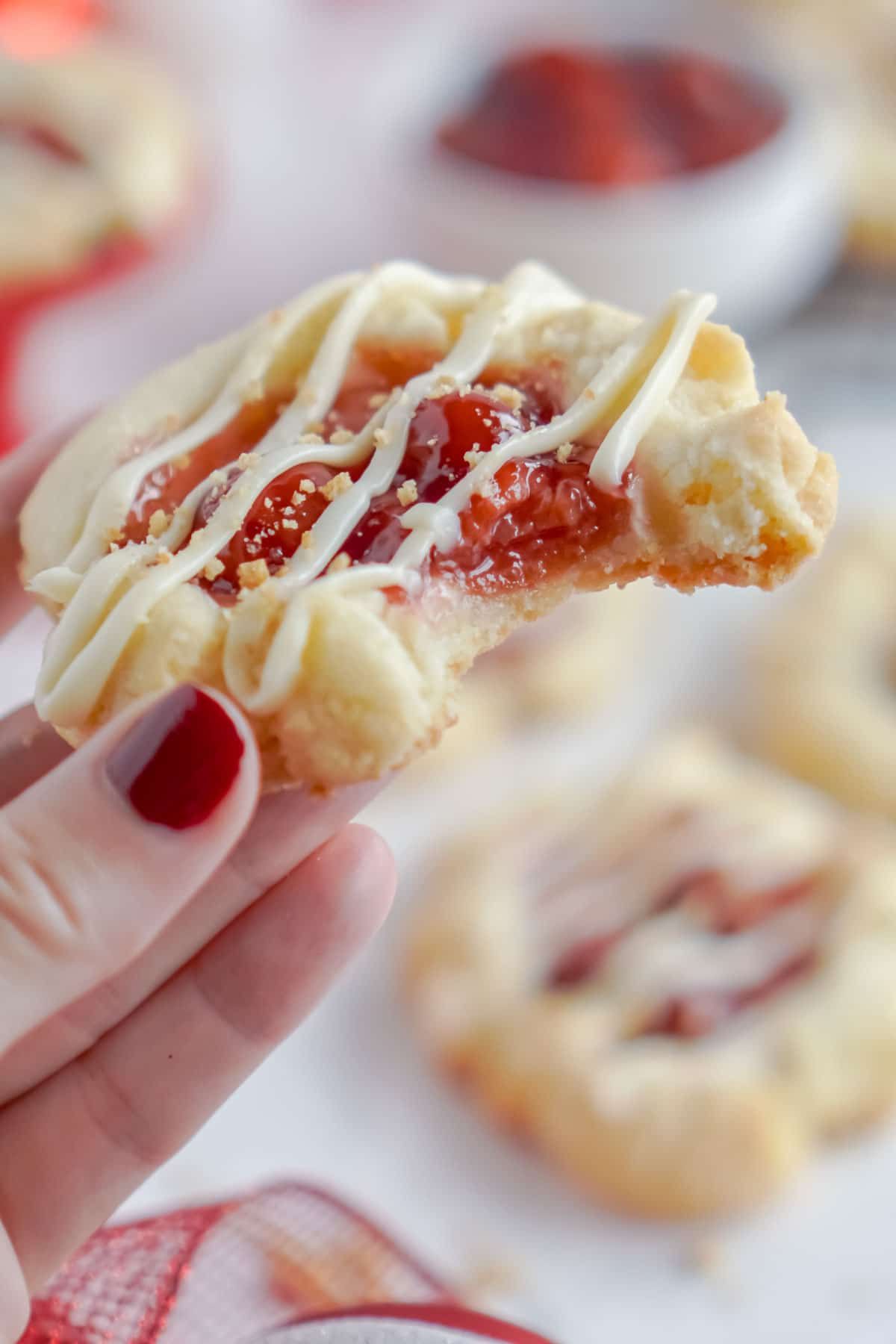 Hånd, der holder en kirsebær cheesecake cookie med en bid taget ud