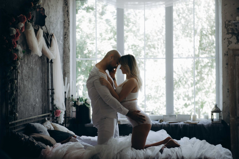   Muž a žena kľačia na posteli vedľa okna