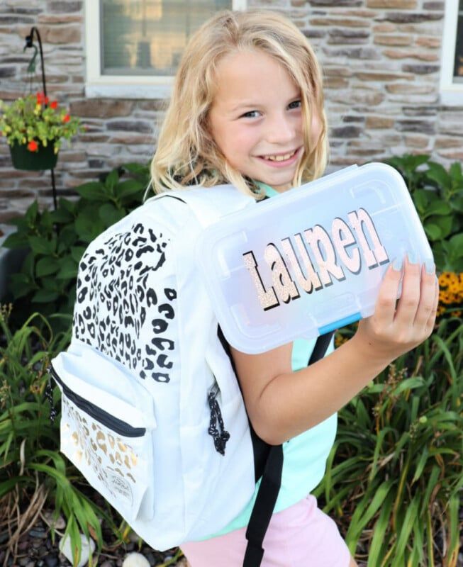 Jeune fille tenant un étui à crayons qui dit Lauren et portant un sac à dos à imprimé léopard