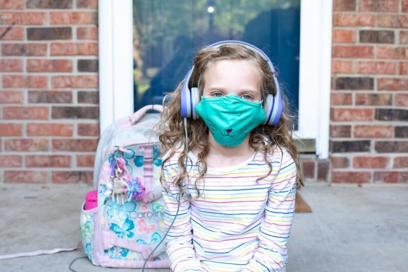 Una niña con una máscara personalizada y sosteniendo una mochila.
