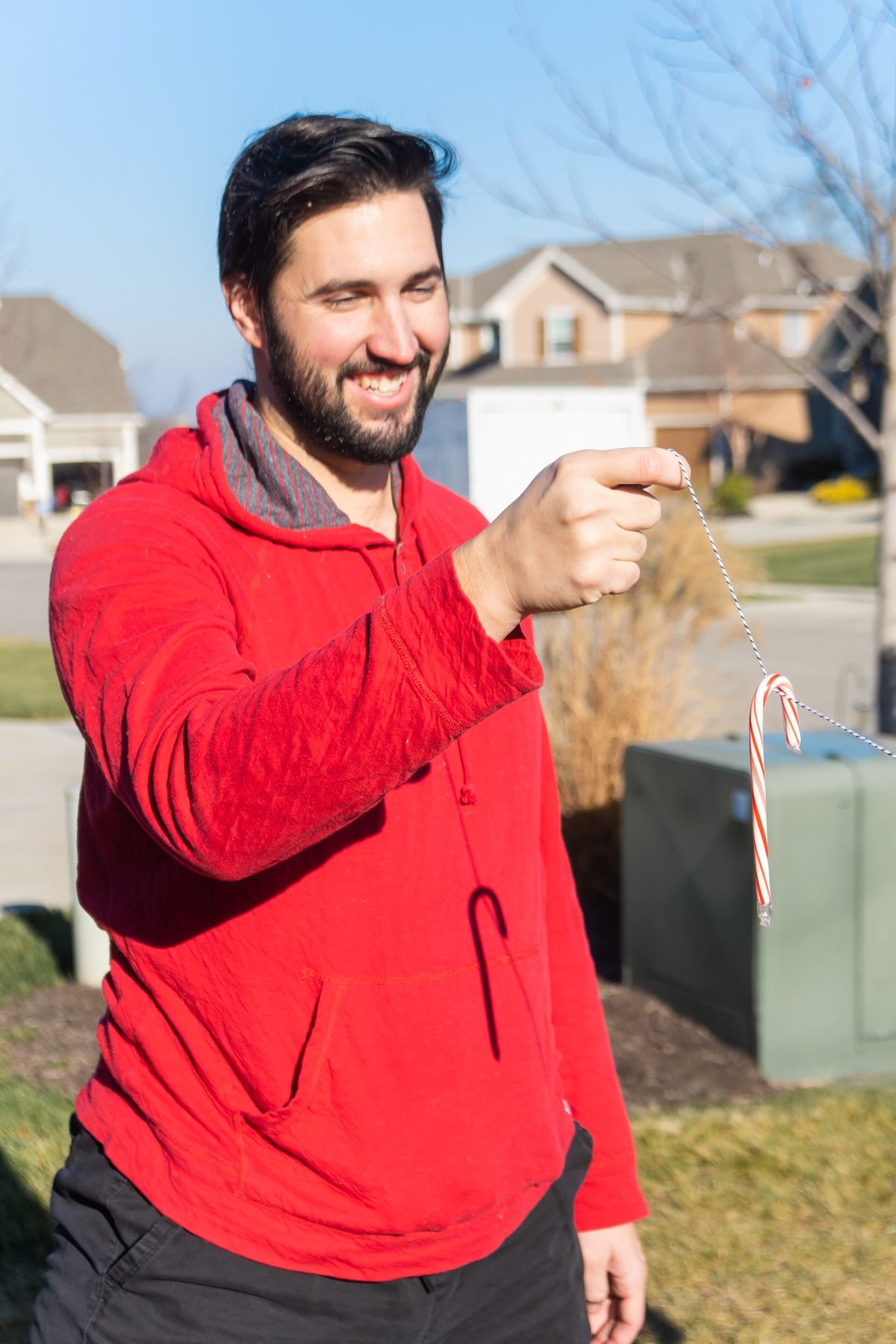 Cilvēks sarkanā sporta kreklā, turot konfektes spieķi uz auklas