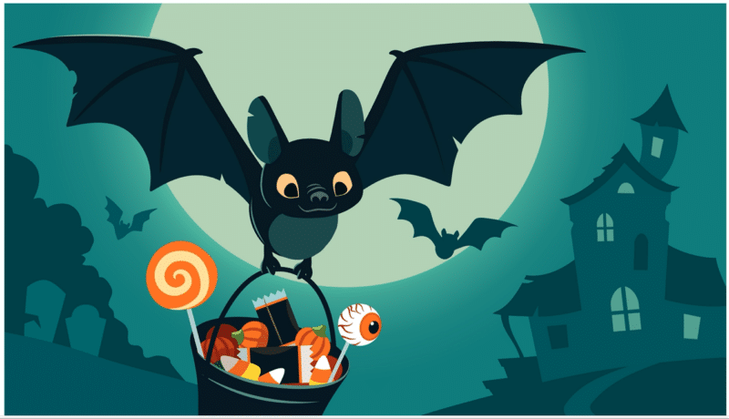 Fotografie netopýra, který drží košík cukrovinek se strašidelným domem v pozadí