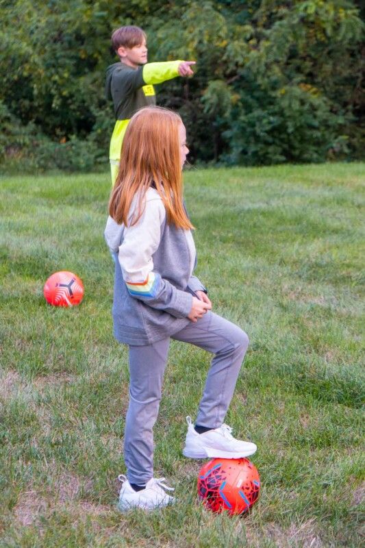 Noia amb el peu sobre una pilota de futbol rosa