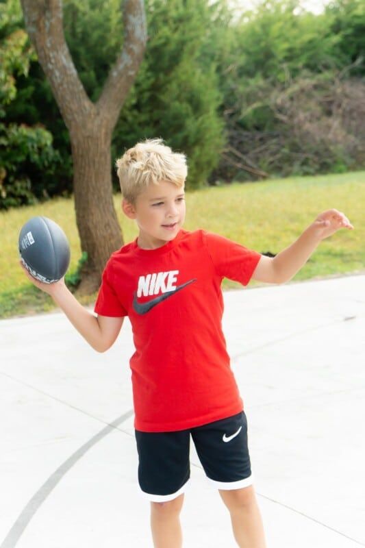 Dítě v červené košili Nike hází fotbal