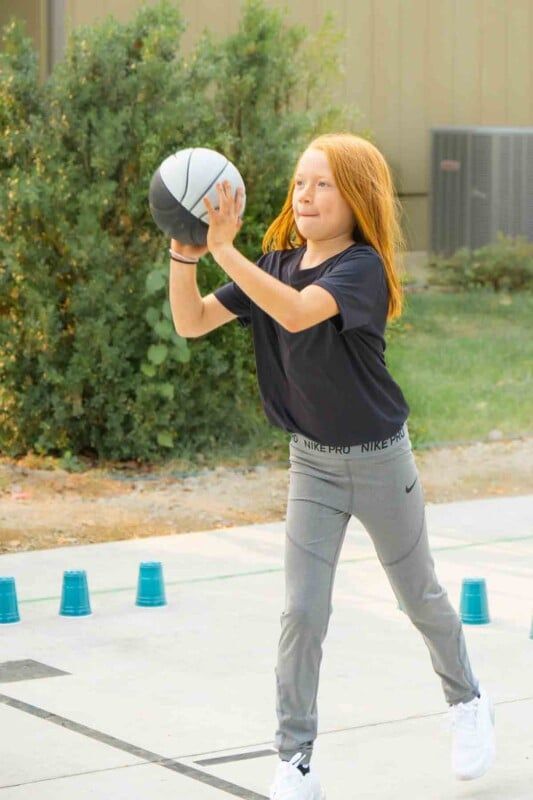 Chica sosteniendo una pelota de baloncesto con vasos de plástico en el suelo