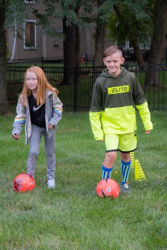 Du vaikai su rausvais futbolo kamuoliais žolėtame lauke