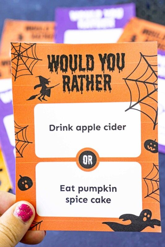 Una mano sosteniendo una tarjeta naranja de Halloween, ¿preferirías cuestionar una tarjeta con brujas y telarañas?