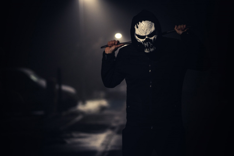   Osoba v černé bundě s bílou děsivou maskou a nesoucí hůl
