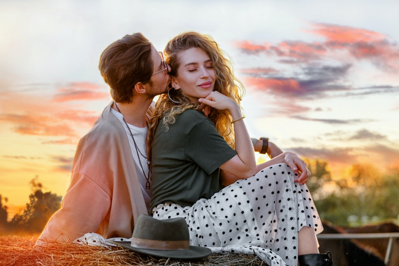   Vyras saulėlydžio metu ant šieno kupetos bučiuojasi su patrauklia mergina