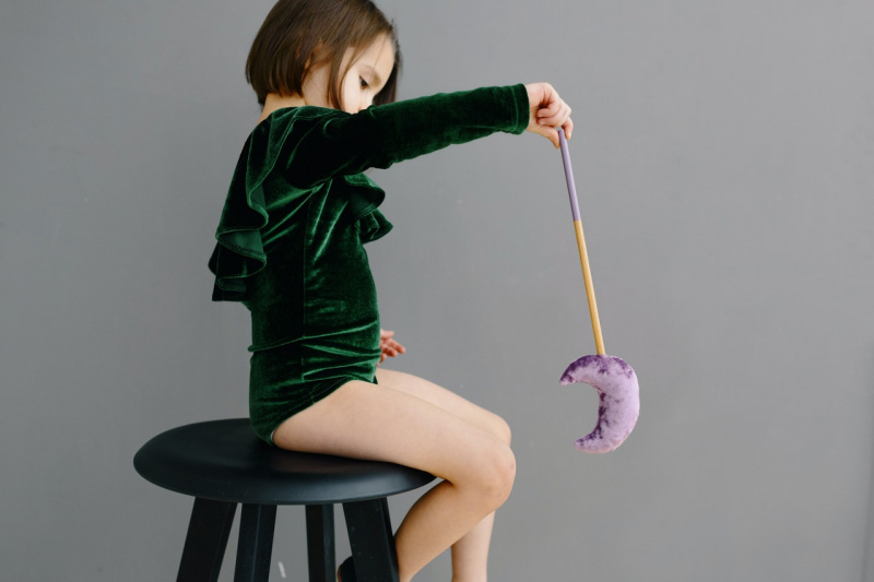   Una noia jove amb body verd asseguda a la cadira mentre sosté un bastó amb una lluna