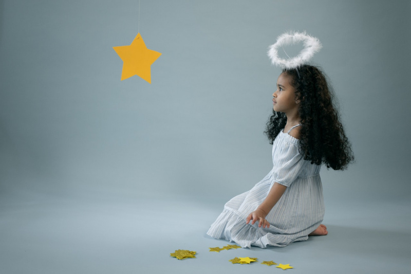  Adorable niña en traje de ángel cerca de estrella colgante