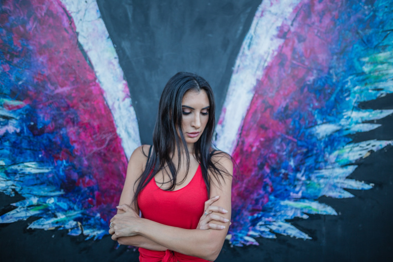   una mujer en vestido rojo de pie contra una pared con alas de ángel