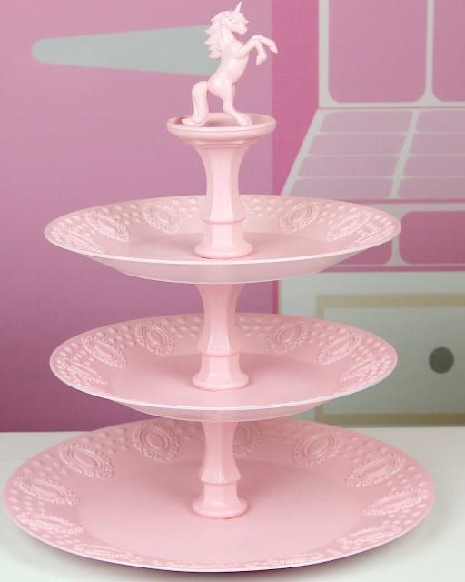 Un soporte rosa para cupcakes con un unicornio encima.