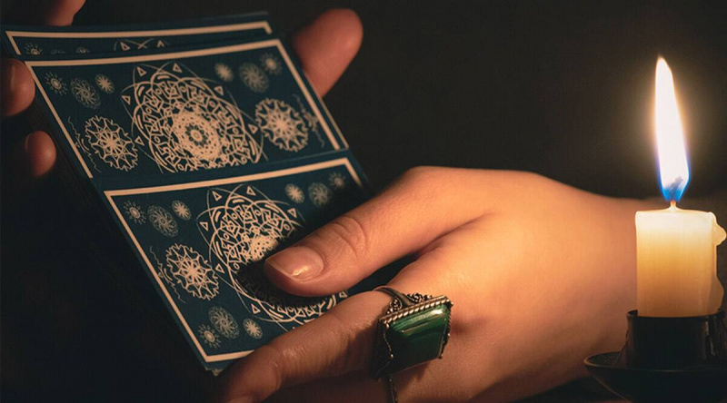   Een persoon met een groene ring die tarotkaarten vasthoudt met een kaars