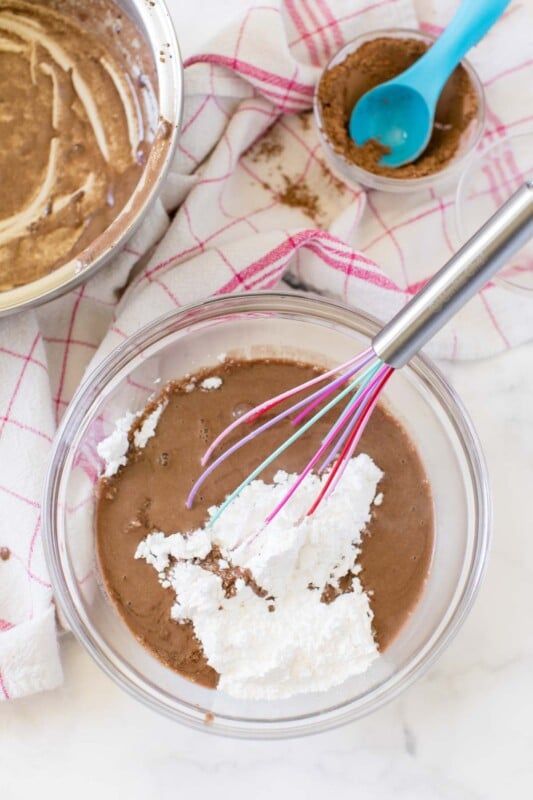 Glaseado de pastel de brownie de chocolate y azúcar en polvo en un tazón con un batidor rosa