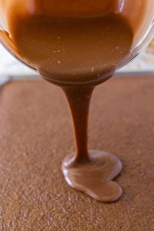 Recipiente de vidrio vertiendo glaseado sobre pastel de brownie de chocolate