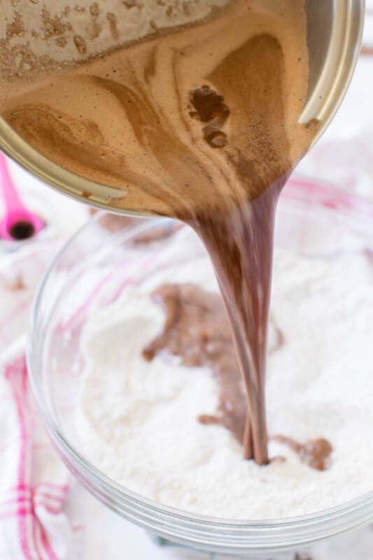 Olla de metal vertiendo la mezcla de chocolate a la mezcla de harina en un tazón de vidrio.