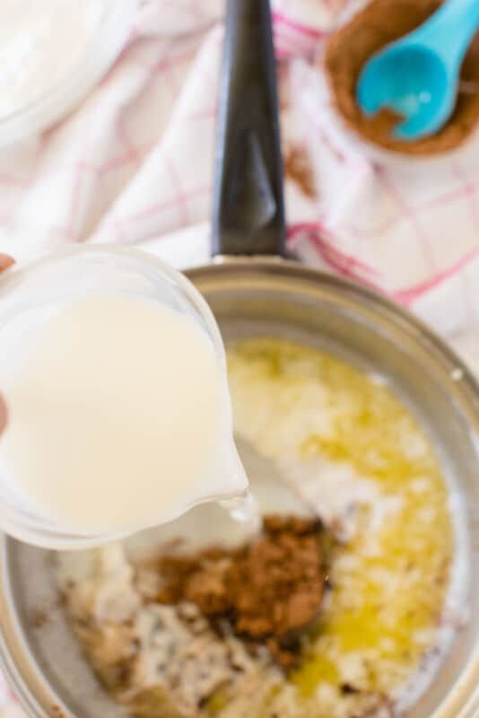 Стъклена мерителна чашка, добавяща мляко към разтопено масло в тенджера