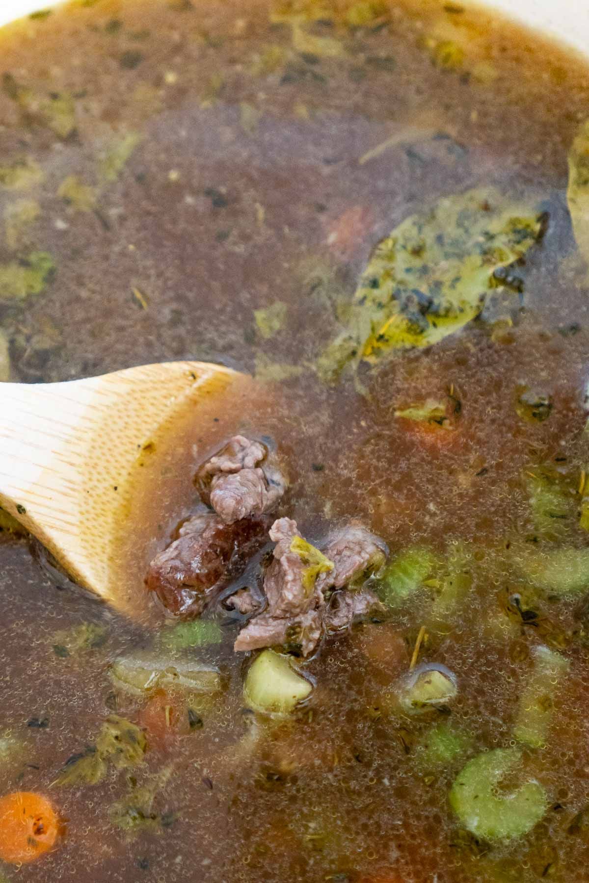 Cuchara de madera revolviendo la carne en una sopa de cebada y carne