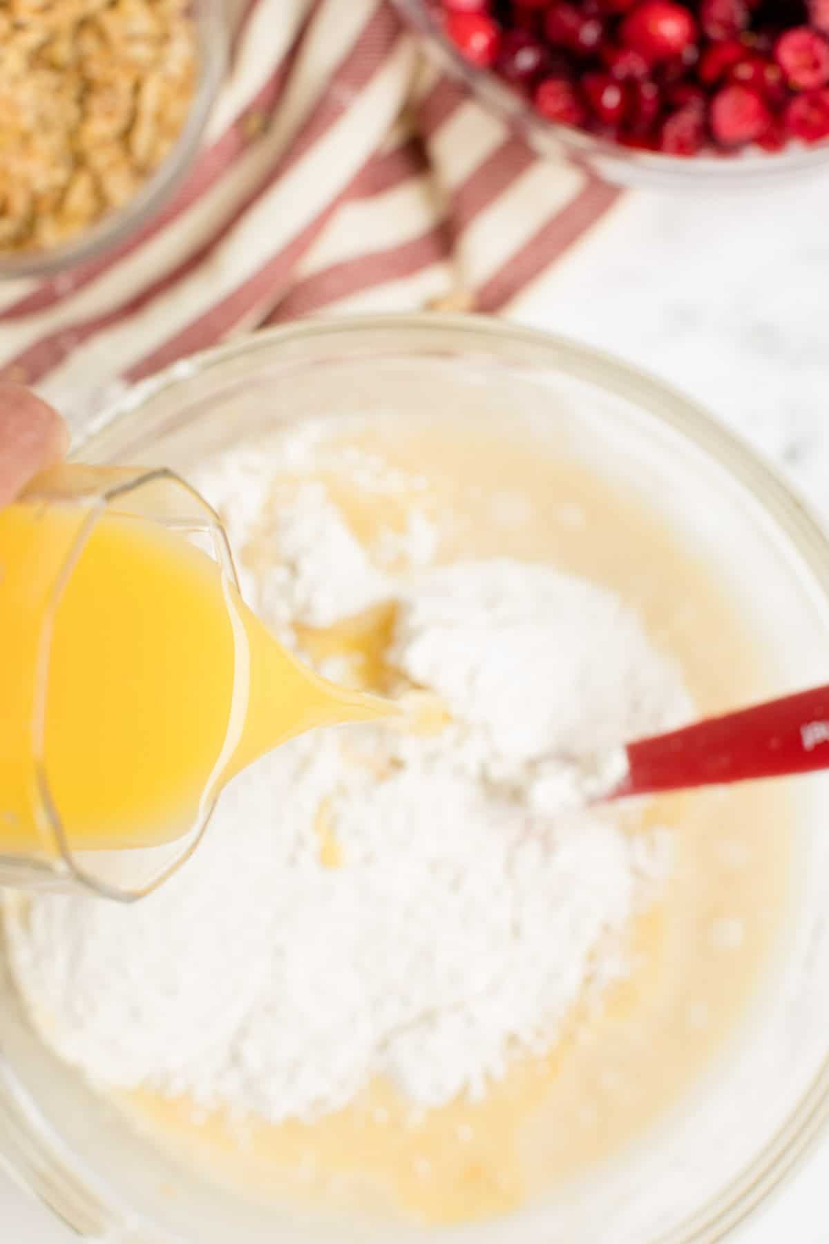 Verter a mano un vaso de jugo de naranja en un recipiente con masa de pan de naranja y arándanos