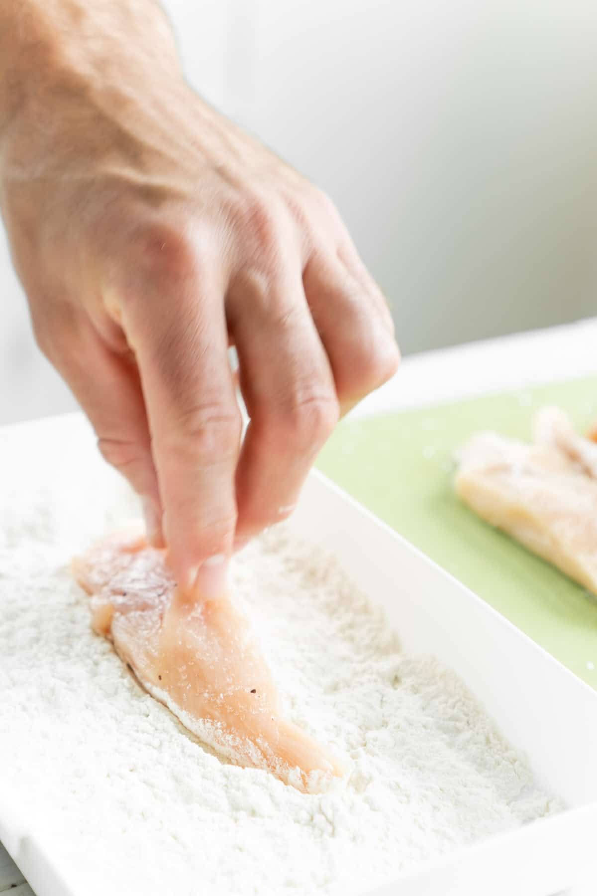 आटे की डिश में चिकन टेंडर डालते हुए हाथ