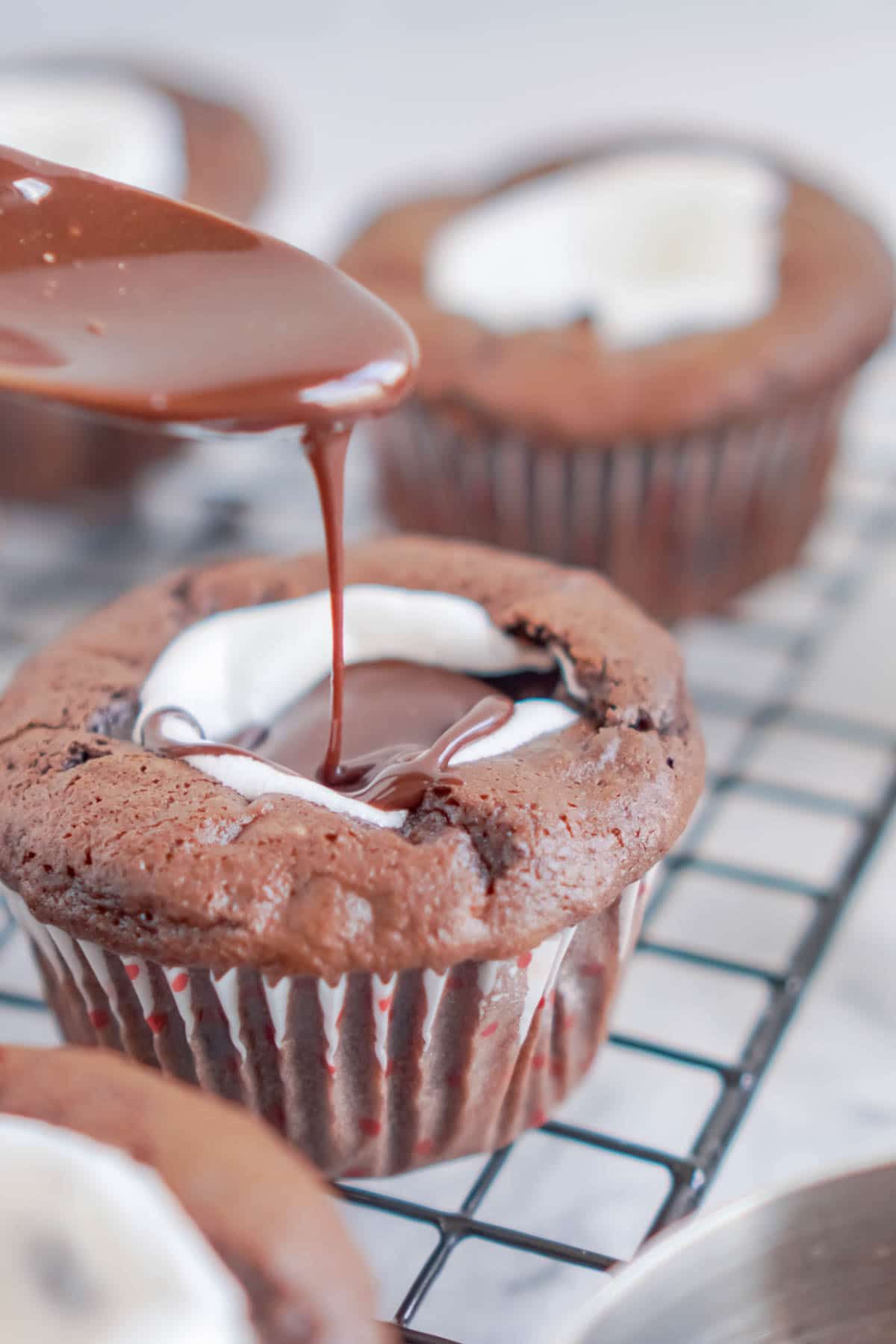 Cuchara vertiendo glaseado de chocolate en cupcakes de chocolate
