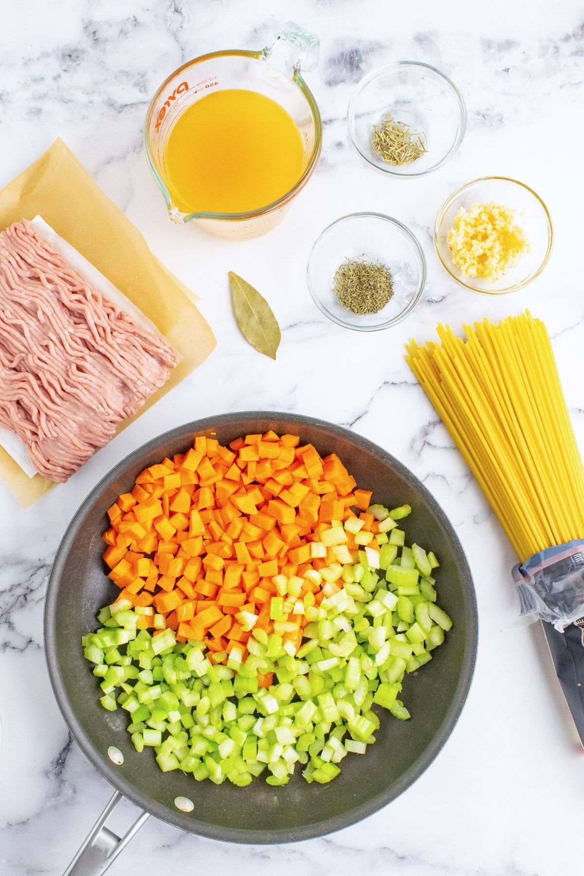 Σέλινο και καρότα σε ένα τηγάνι με άλλα συστατικά για αλεσμένα ζυμαρικά γαλοπούλας γύρω του