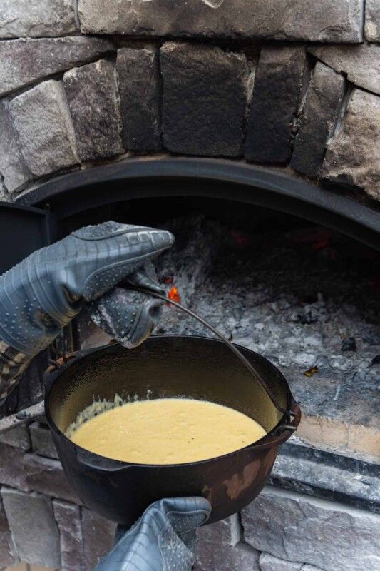 Tangan sarung tangan oven memasukkan ketuhar adunan roti jagung ke dalam oven bata