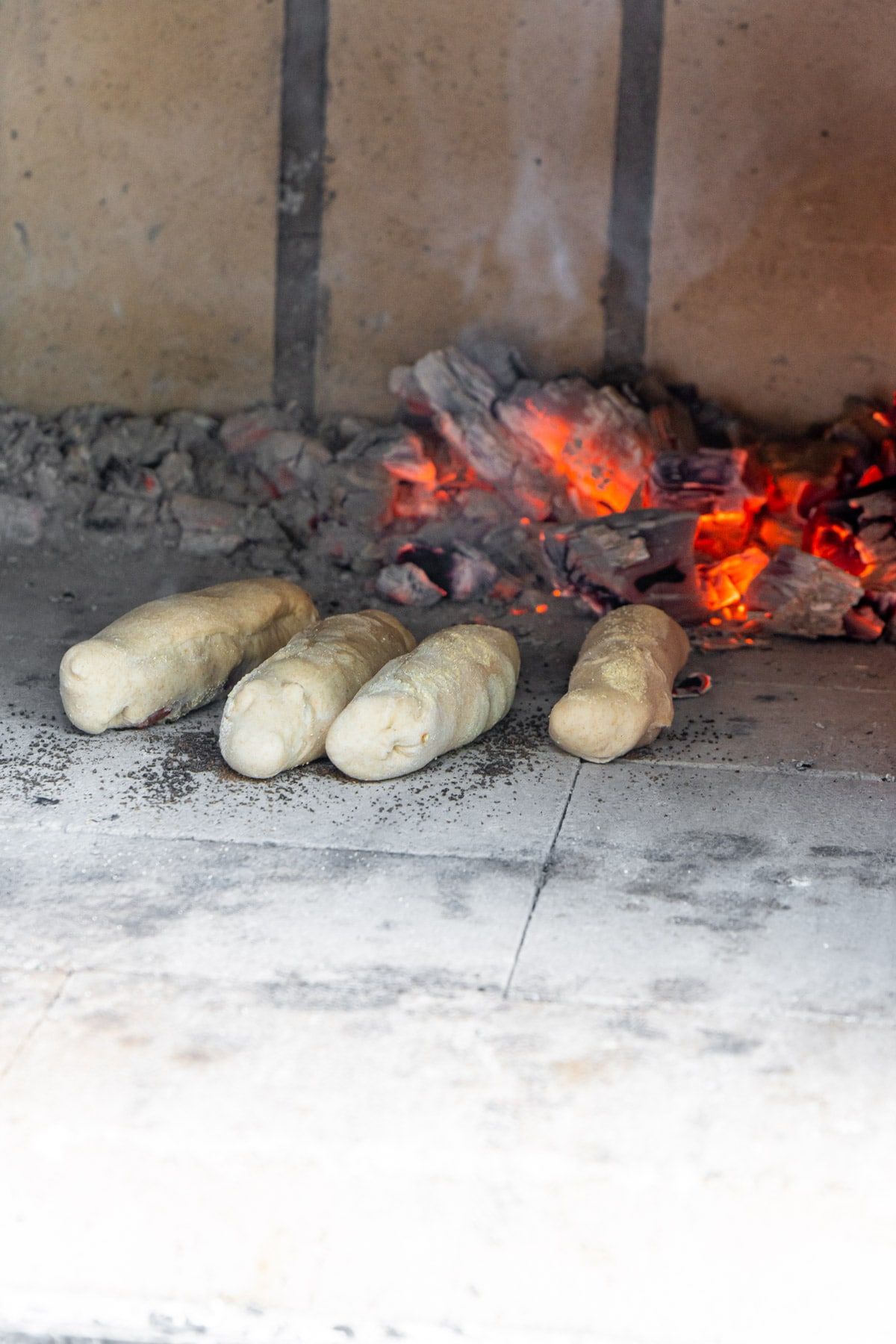 Τέσσερα ρολά πεπερόνι σε φούρνο από τούβλα με φωτιά στο παρασκήνιο