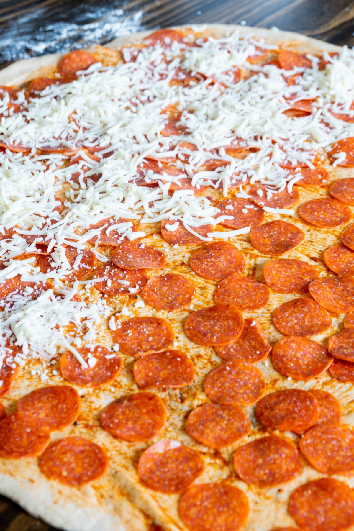 Masa de pizza grande extendida cubierta con pepperoni y salsa