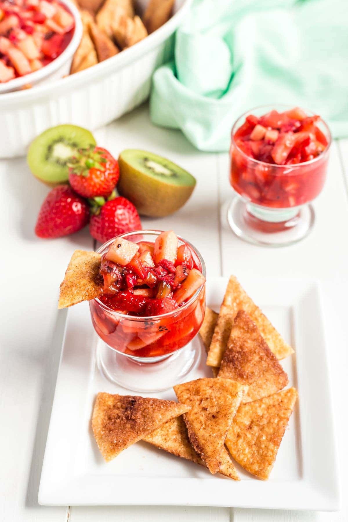 Ένα μικρό ποτήρι salsa φρούτων σε ένα πιάτο με τα τσιπ κανέλας και το salsa φρούτων στο υπόβαθρο
