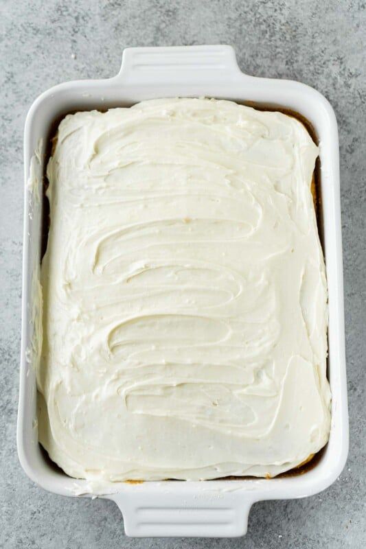 Un pastel con glaseado cremoso blanco en un molde rectangular blanco
