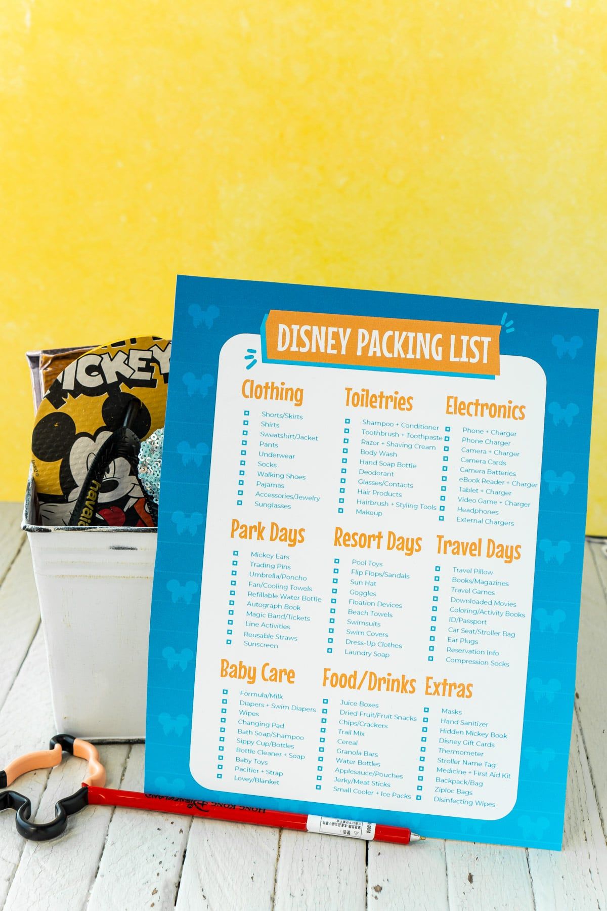 Balicí seznam Disney před kbelíkem plným předmětů Disney se žlutým pozadím