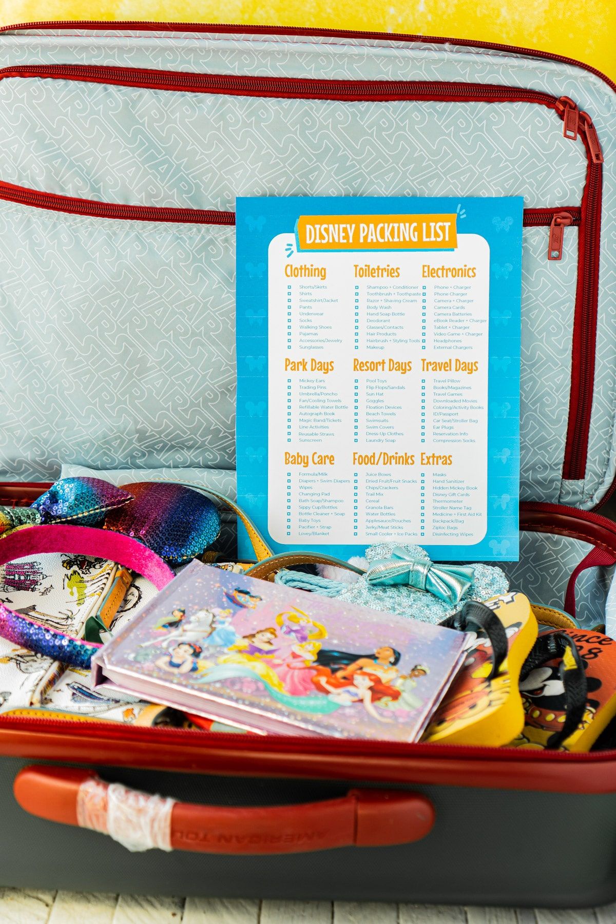 Lista de embalagem da Disney em cima de uma mala cheia de itens Disney